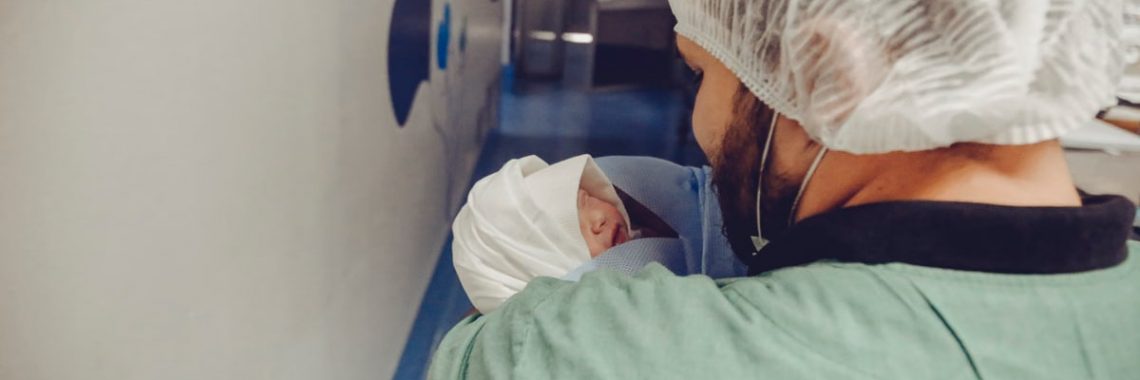 Healthcare worker holding a newborn baby in a hospital hallway, showcasing care and professionalism.