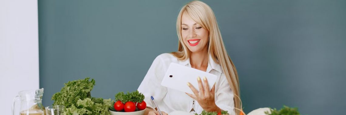 Woman using a tablet surrounded by fresh vegetables at a table, showcasing healthy lifestyle and technology.